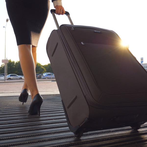 Lower body shot of a woman in high heels rolling a traveling suitcase 