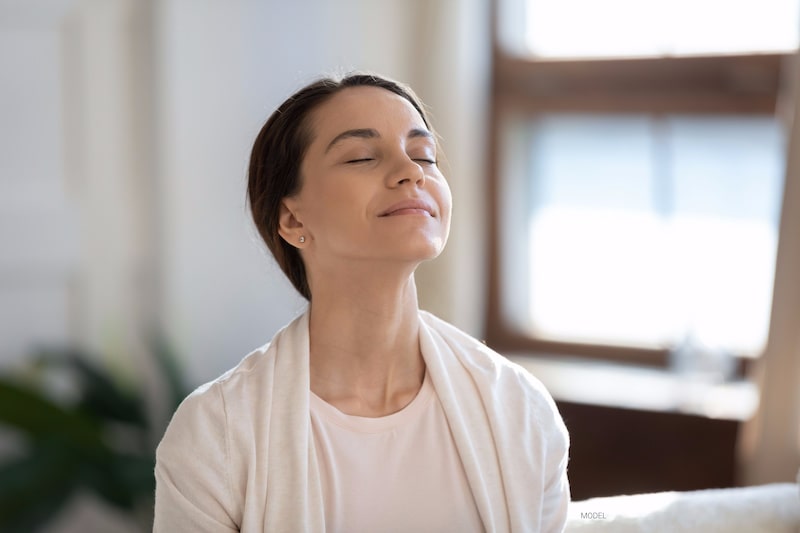 Beautiful young woman taking a deep breath in while looking calm and content