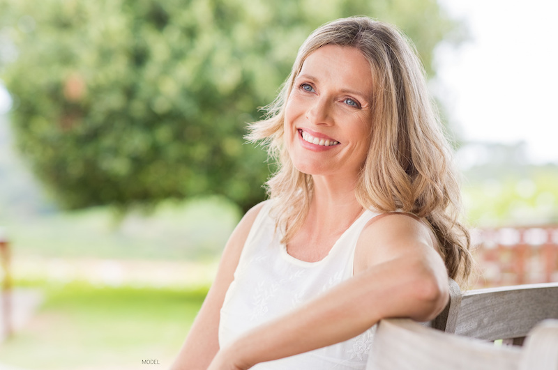 Blonde woman sitting on a chair outside.