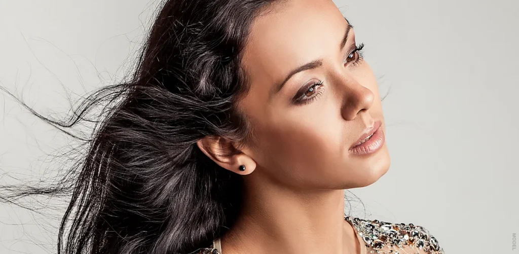 A hispanic woman against a light grey background with her long hair blowing.